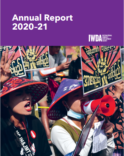 The header at the top of the page is white text on a purple background reading: Annual Report 2020-2021, alongside the IWDA's logo also in white text. Below the header is an image fills the rest of the page. It depicts women speaking into a megaphone at a rally in Myanmar.