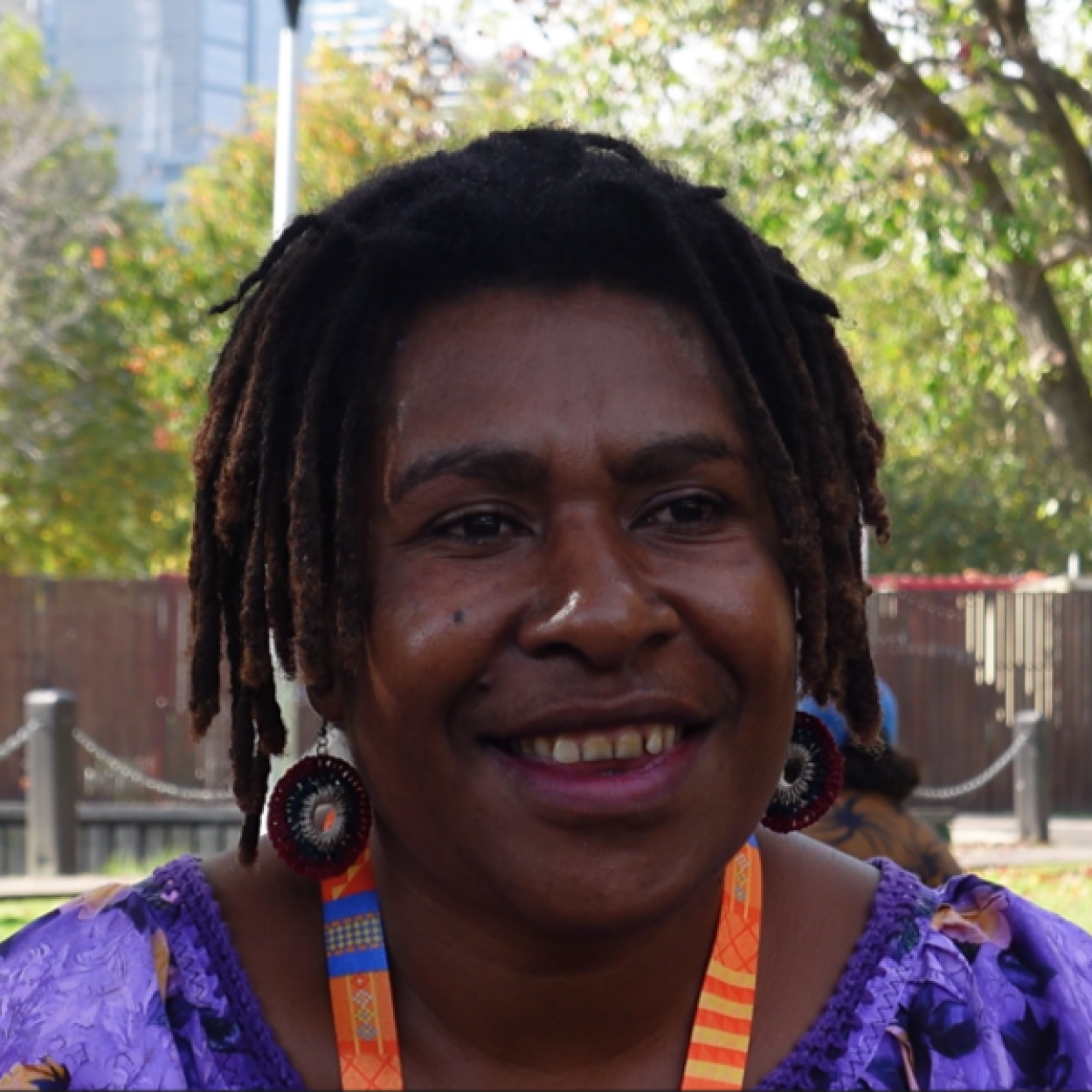 photo of Clara, a woman from PNG smiles at the camera, wearing orange lanyard and purple dress.