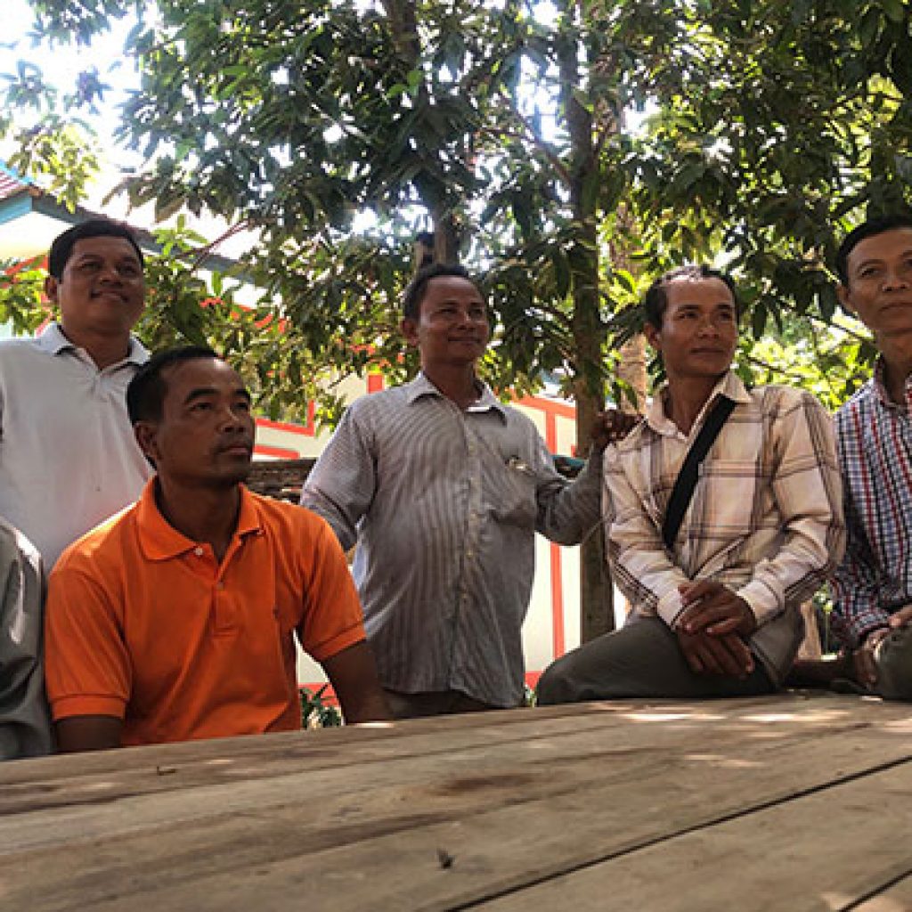 Members of Banteay Srei's Good Men's Network sit together below trees