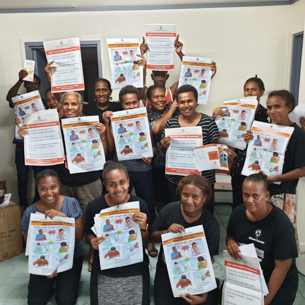 A group of fourteen men and women from the family support centre in the Solomon Islands hold up posters