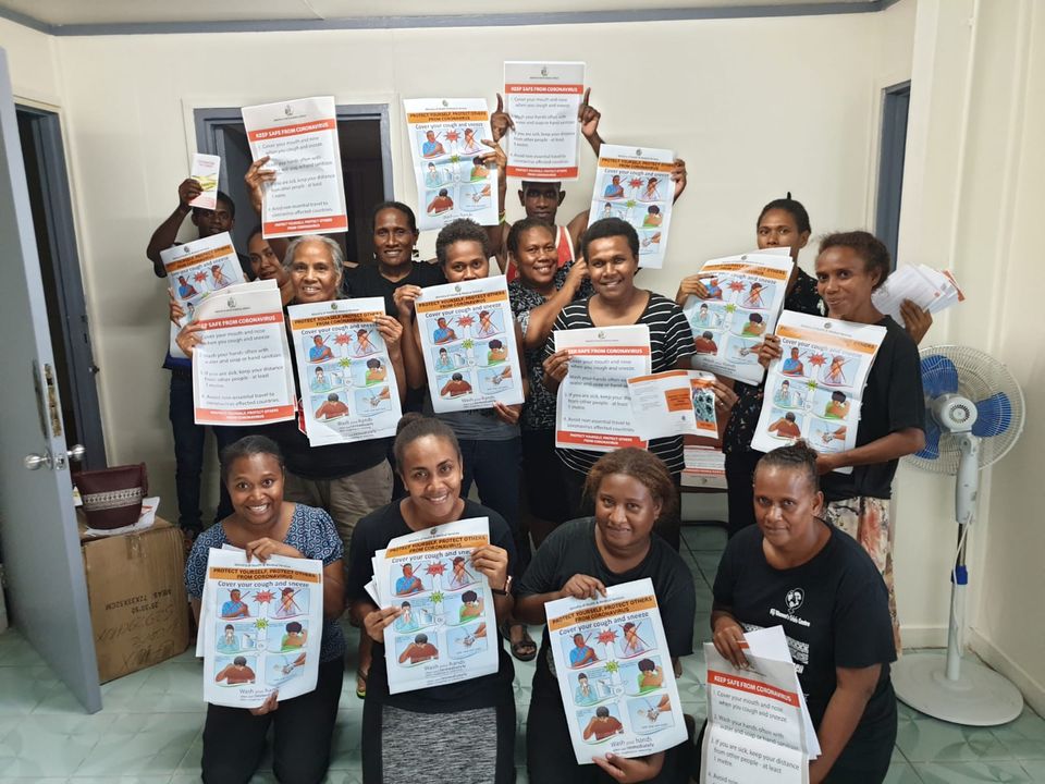 A group of fourteen men and women from the family support centre in the Solomon Islands hold up posters