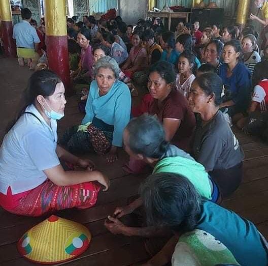 A woman seated with a large group, listening to them speak