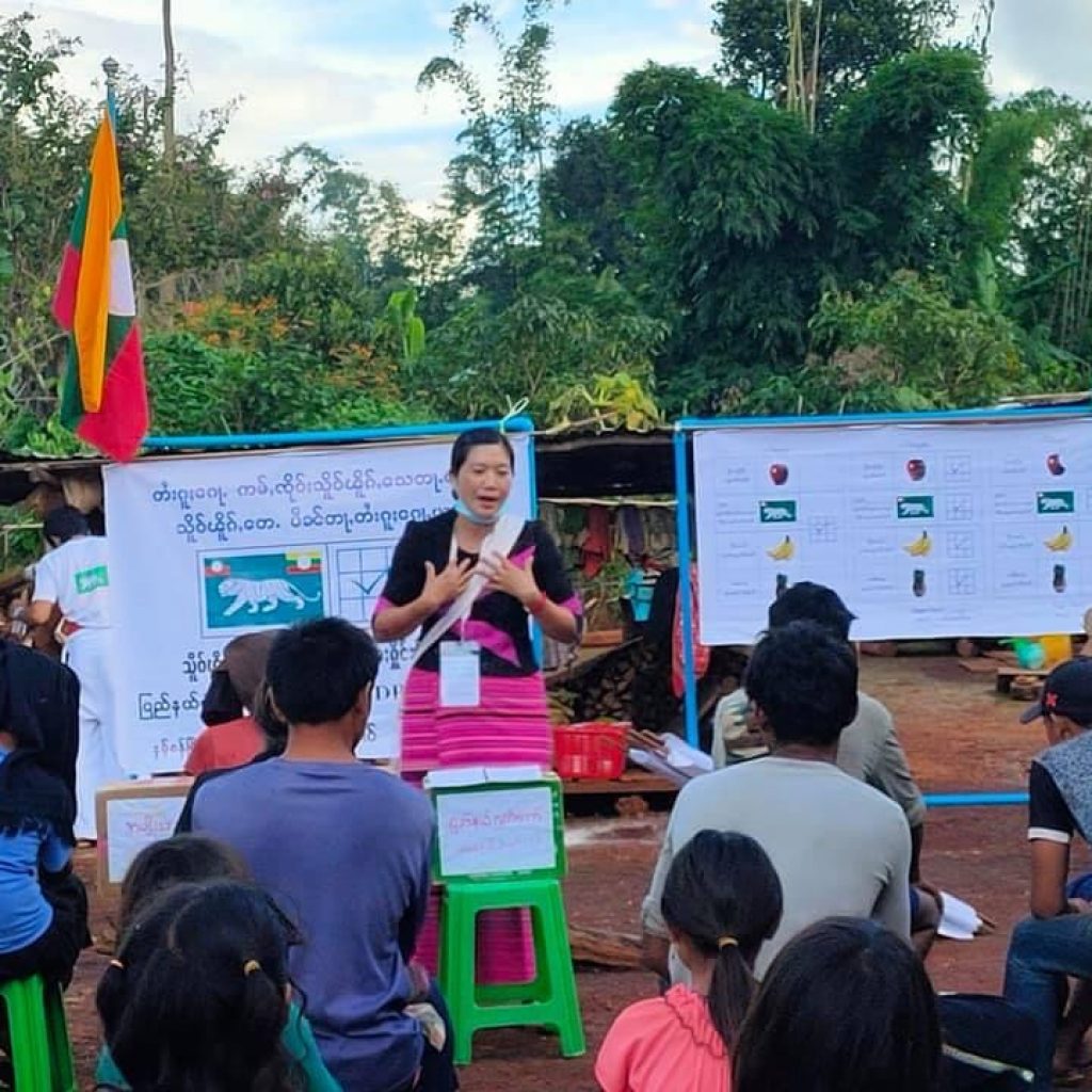 A woman stands and speaks to a group of seated people