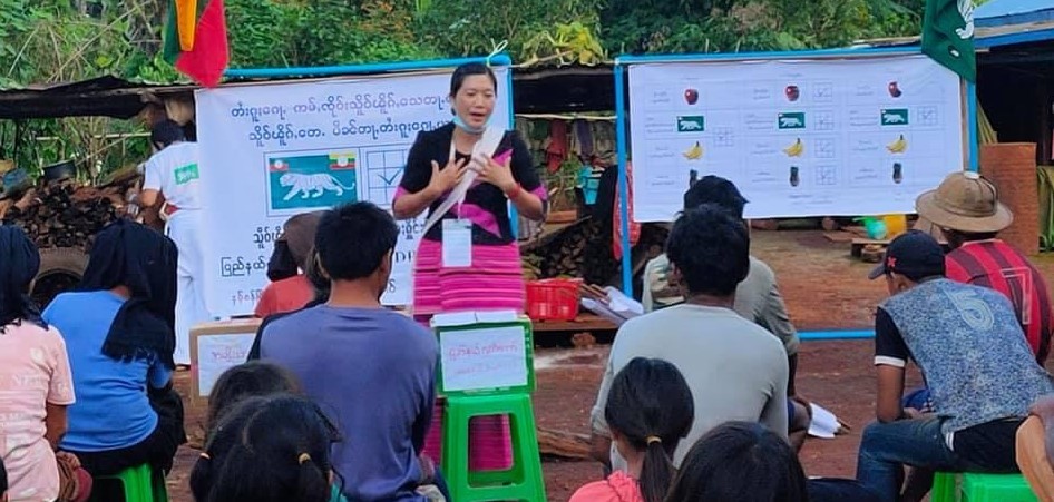 A woman stands and speaks to a group of seated people