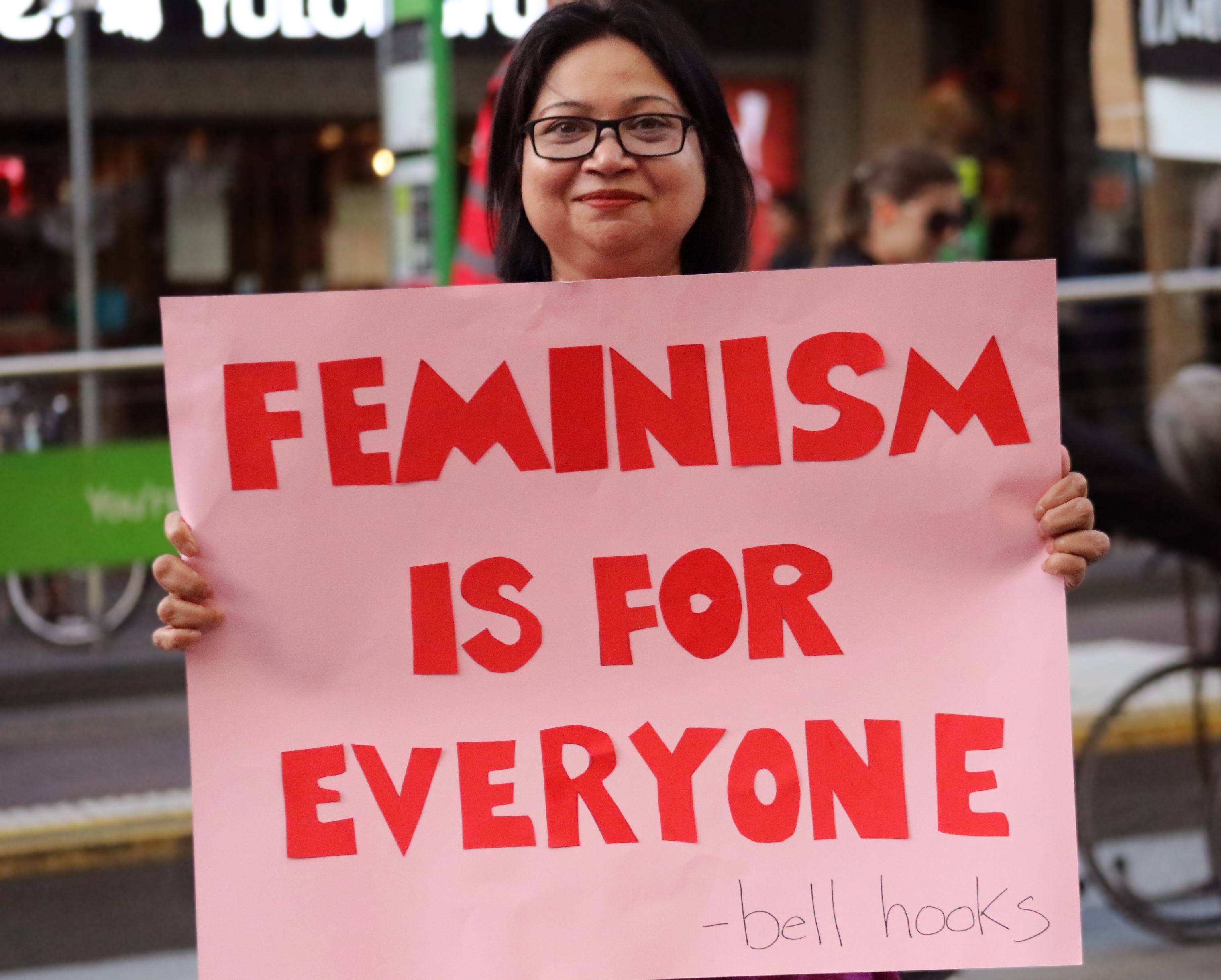 IWDA CEO Nayomi Kannangara at protest holding a pink sign with red lettering. It reads Feminism is for everyone - Bell Hooks. 