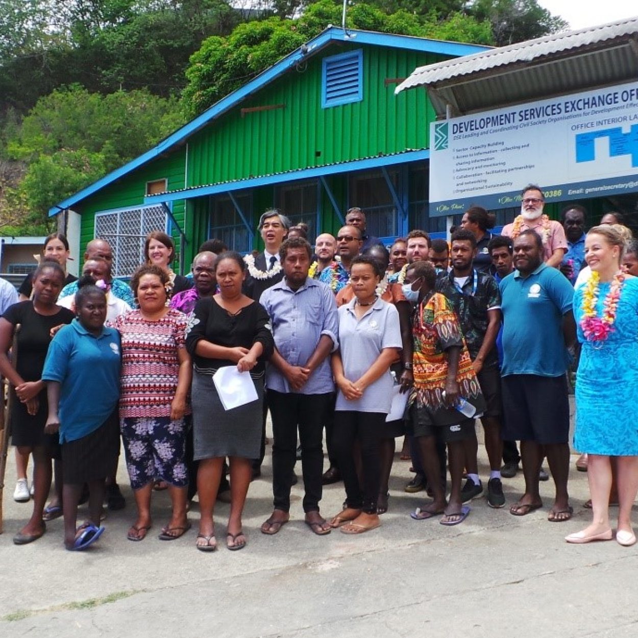 A group of people pose for a photo outside a green and blue office building in Solomon Islands.