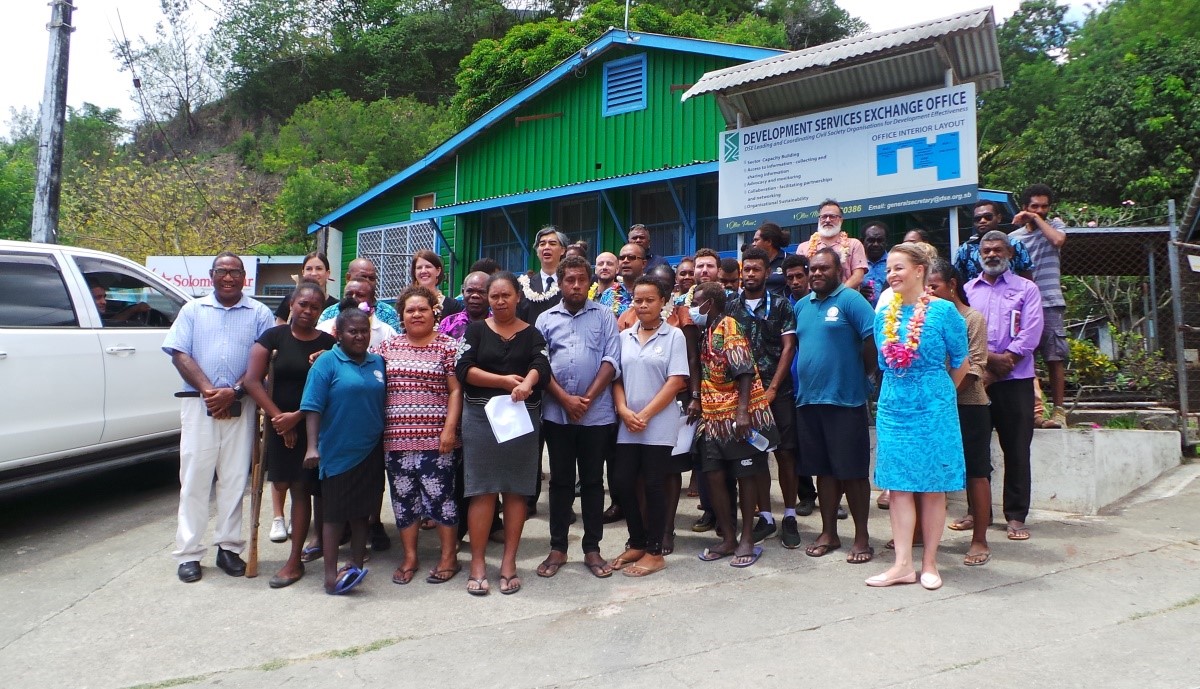 A group of people pose for a photo outside a green and blue office building in Solomon Islands.