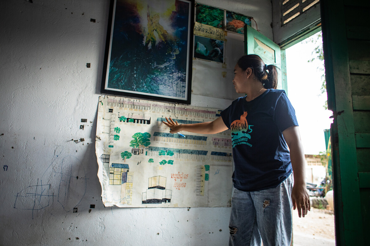 Sreymom, an organiser from WIC is pointing at a poster displayed at one of their drop-in centres. The poster is a drawing of the grounds where the drop-in centre is located included the quarters where factory workers live.