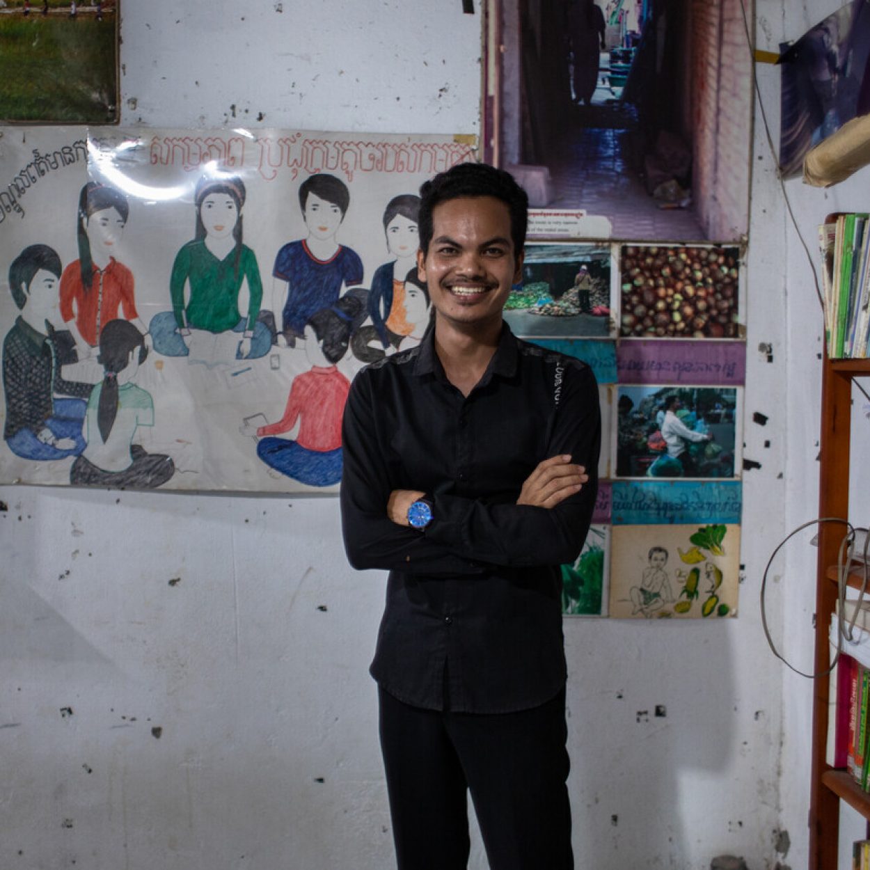 Chorn Phorn, a key organiser at WIC, is posing for the camera during a visit to one of WIC's drop-in centres in Phom Penh. He smiling and standing in front of a poster he created for one of WIC's campaigns.