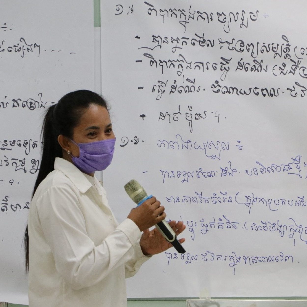 A person is wearing a face mask and speaking into a handheld microphone