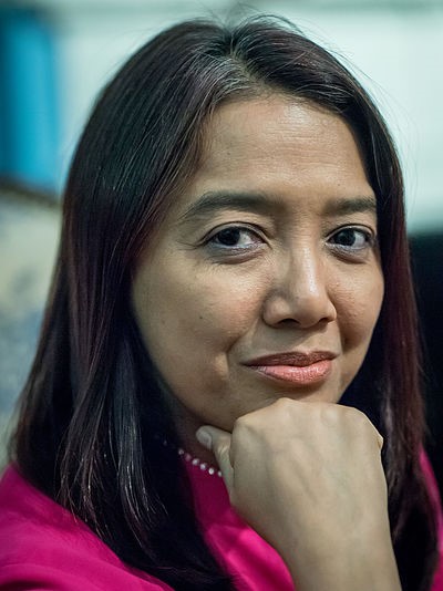 A photo of Myanmar activist Thin Thin Aung. It is a close up portrait of her. Her head is gently resting on her closed fist and as she looks into the camera with a closed-mouth smile.