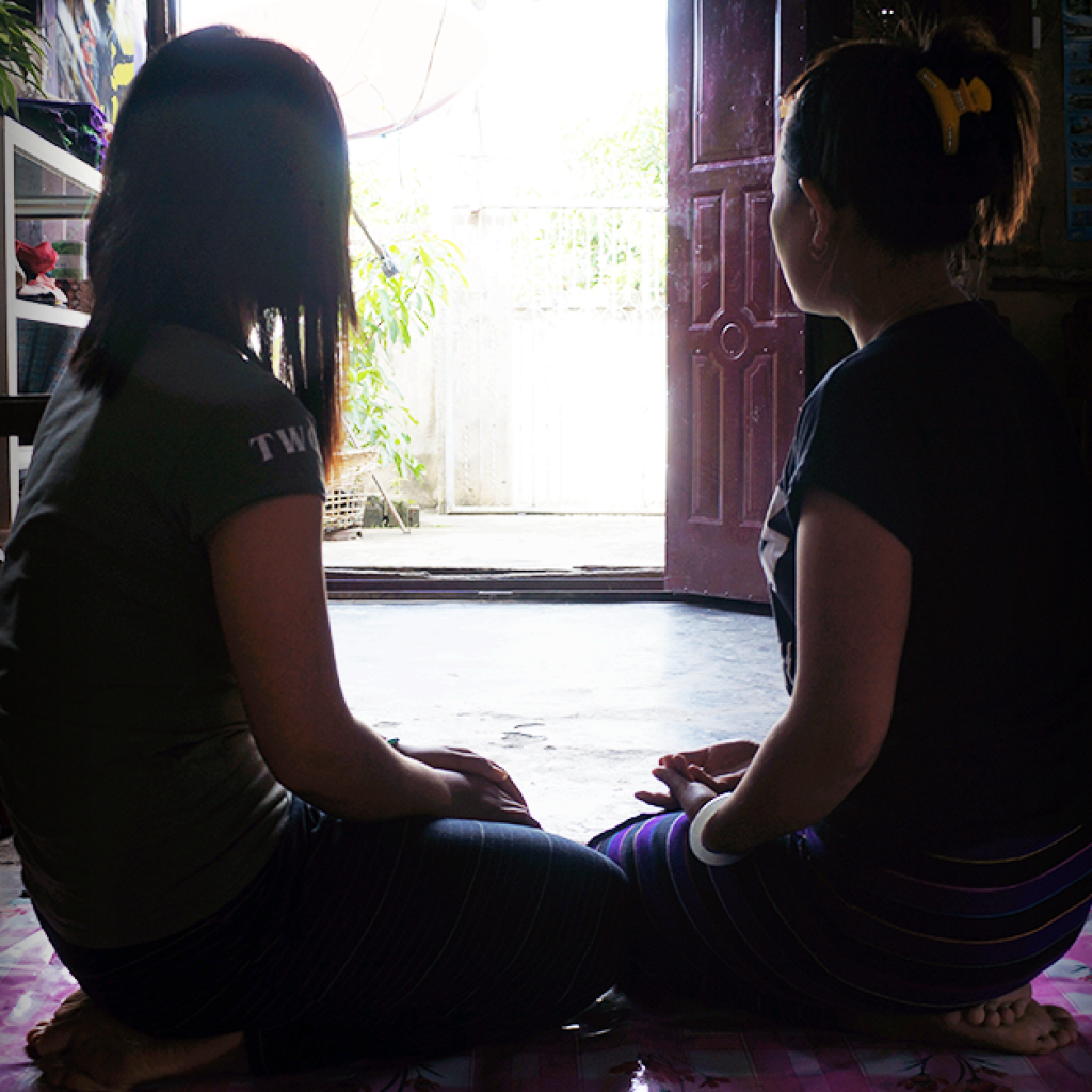 Image of two women in Myanmar sitting on a mat, looking into the distance.