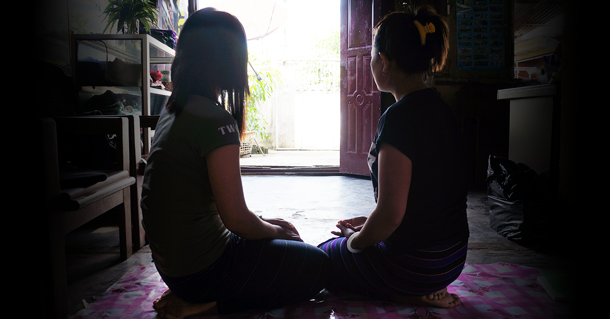 Image of two women in Myanmar sitting on a mat, looking into the distance.