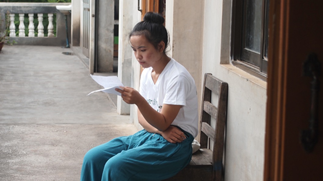 Image of a woman sitting in a hallway, reading a piece of paper.