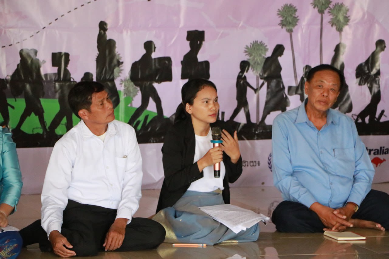 Two men are seated on either side of a woman, listening as she speaks into a microphone.