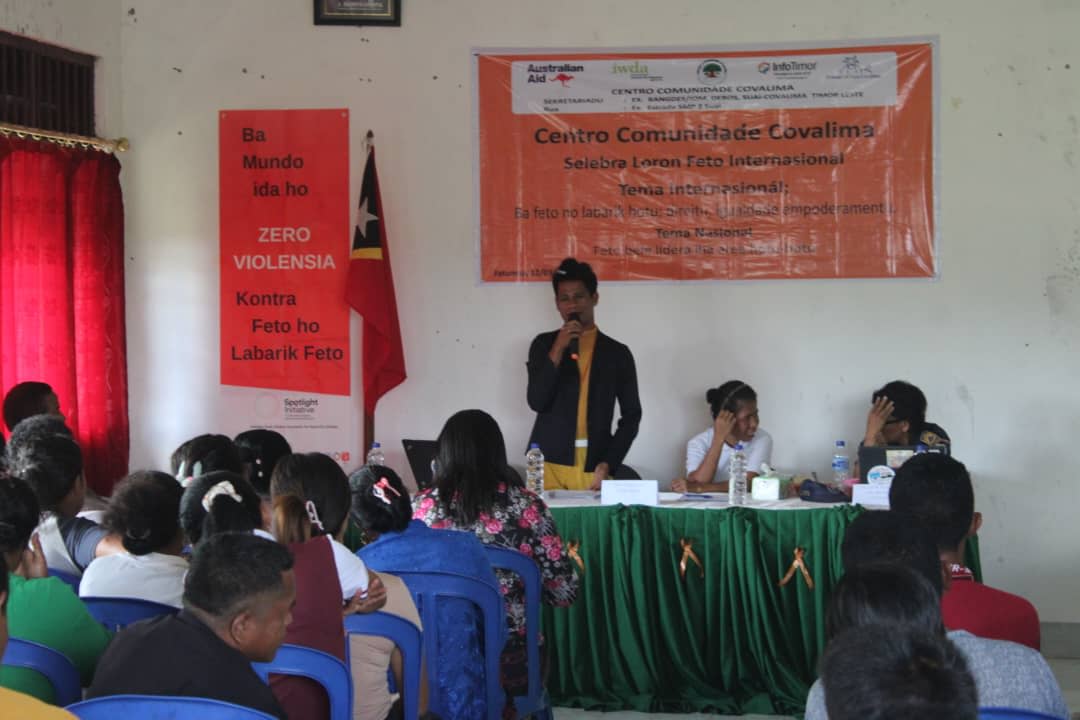 People are gathered in a room for CCC's awareness-raising session. A person is standing at a desk set up in front of the room as they address the crowd through a microphone. 