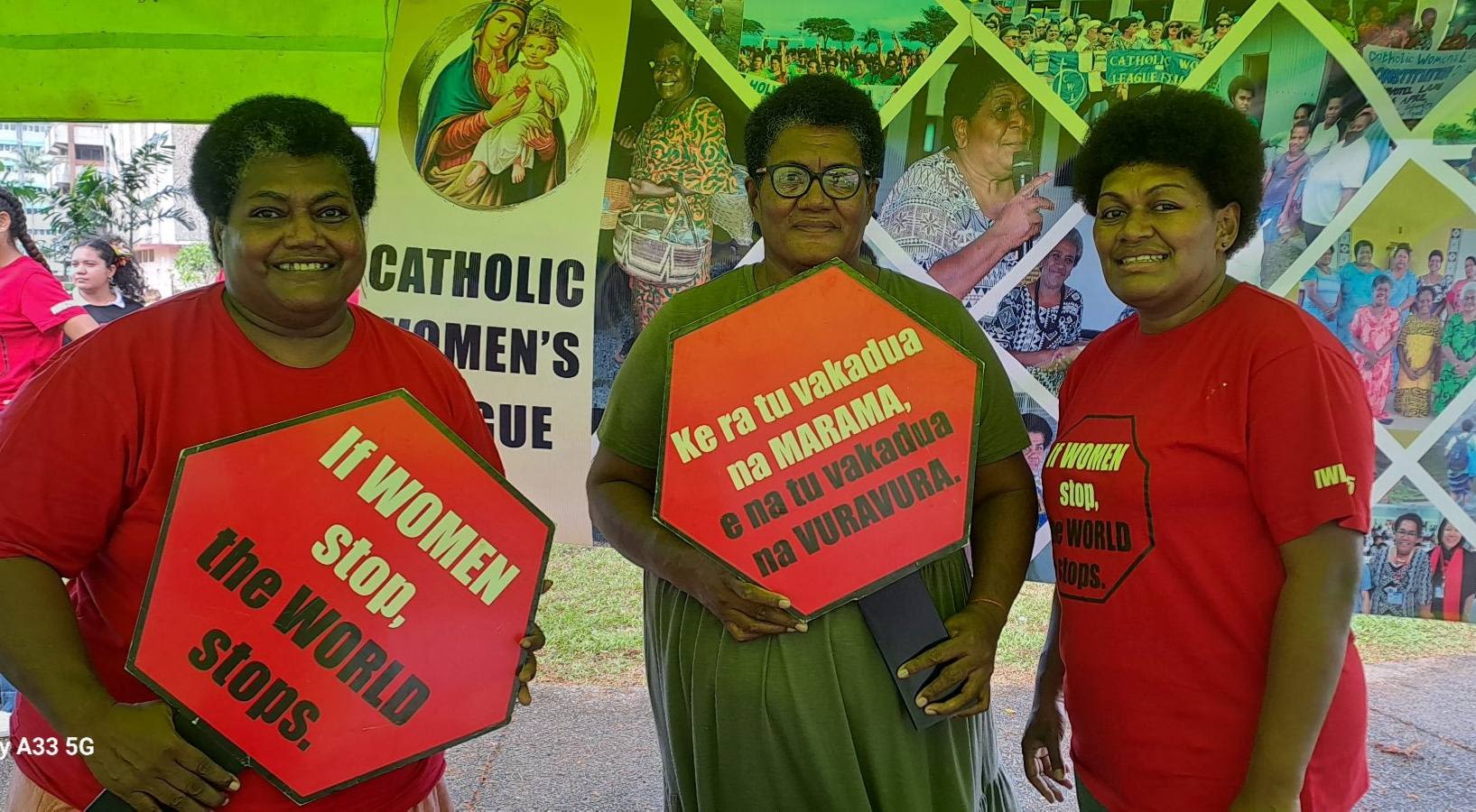 Three women pose togther for the camera as they hold up 'If Women Stop, the World Stops' signs.
