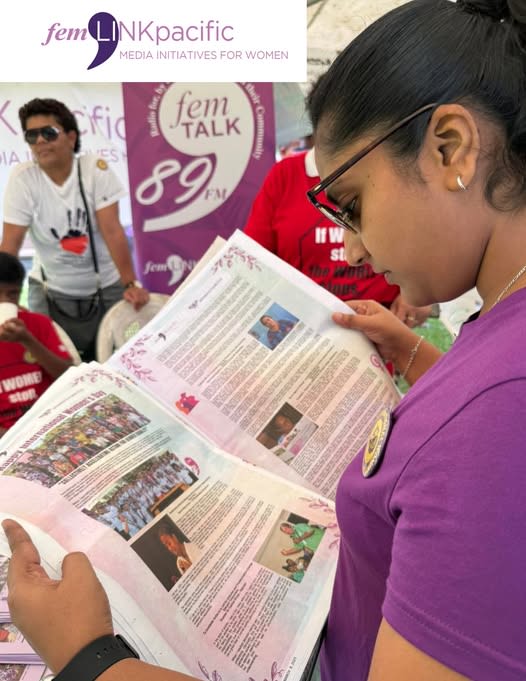 A woman is holding a newspaper as she reads articles written by femLINKpacific for International Women's Day.