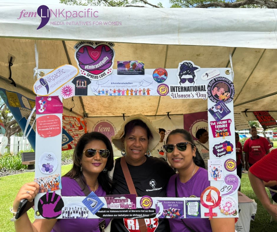 Three women are posing together with a photo frame as they smile at the camera.