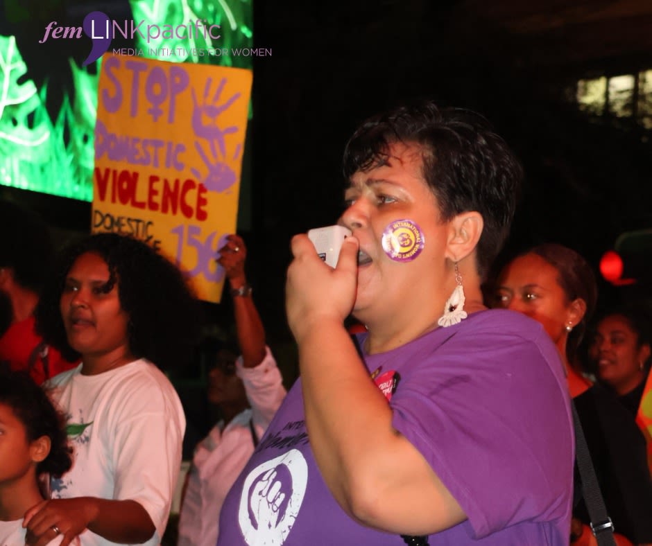 A woman at the Reclaim the Night march is speaking into a megaphone. Behind her is a sign that reads, 'Stop domestic violence.'