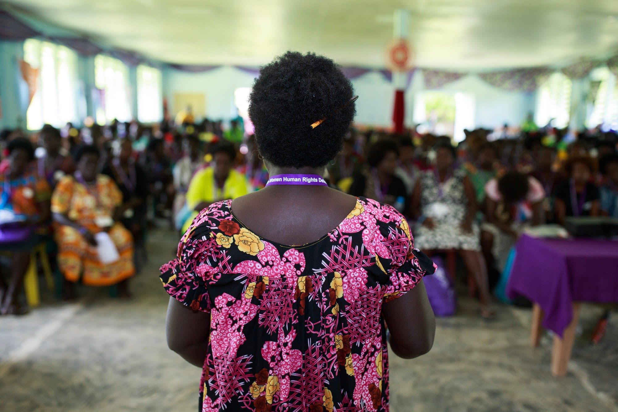 A Woman Human Rights Defender from Bougainville has her back to the camera as she addresses a large crowd gathered in front of her.