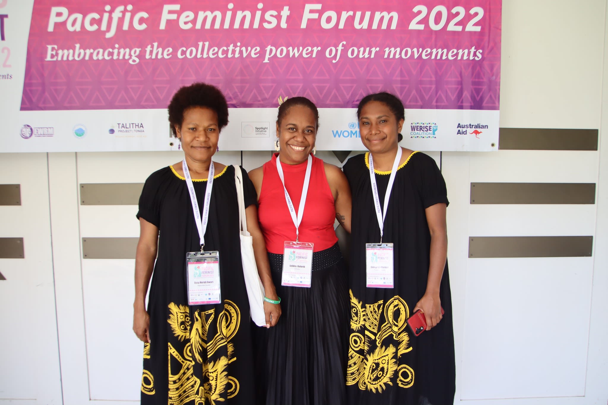 Three women are posing together in front of a forum banner that reads 'Embracing the collective power of our movements.'
