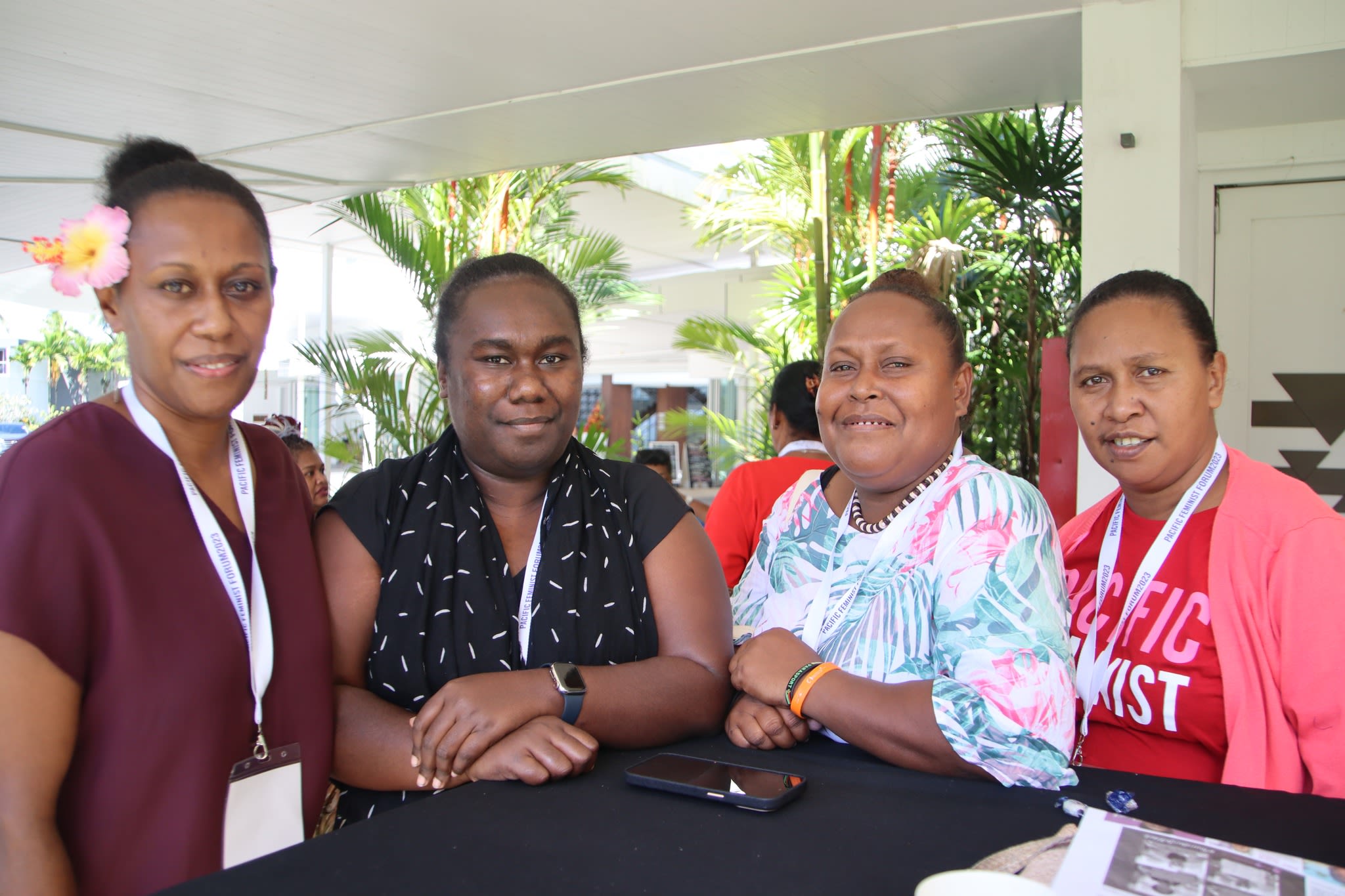 Four women are posing together around a table in an outdoor space at the forum.