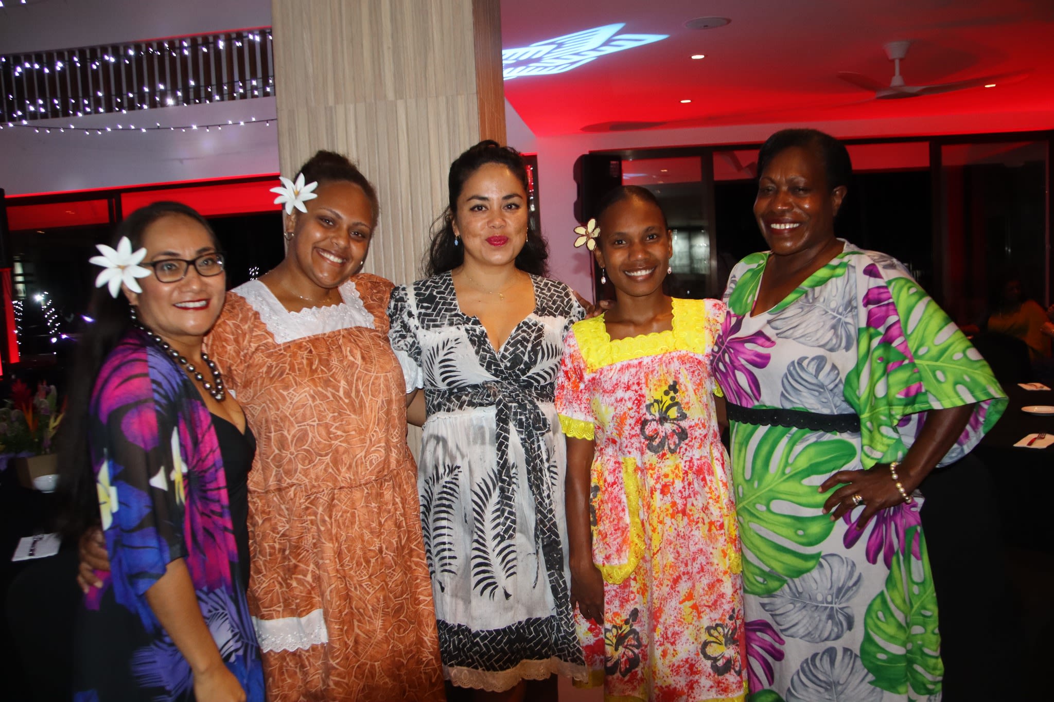 Five women post together for the camera. It is nighttime and they are standing in a room lit up with fairy lights.