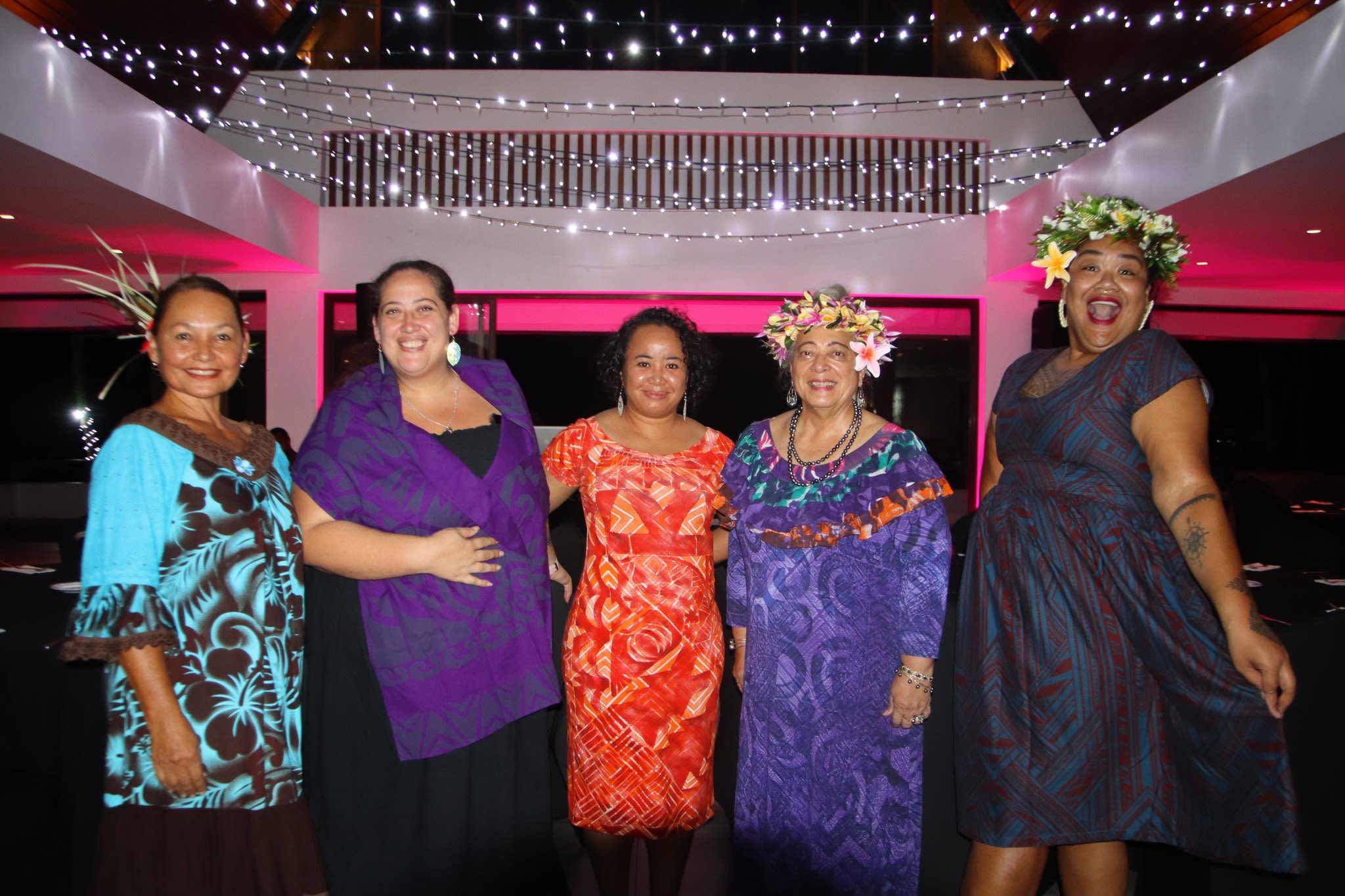 Five women pose together for the camera. It is nighttime and they are standing in a room with fairy lights above them.