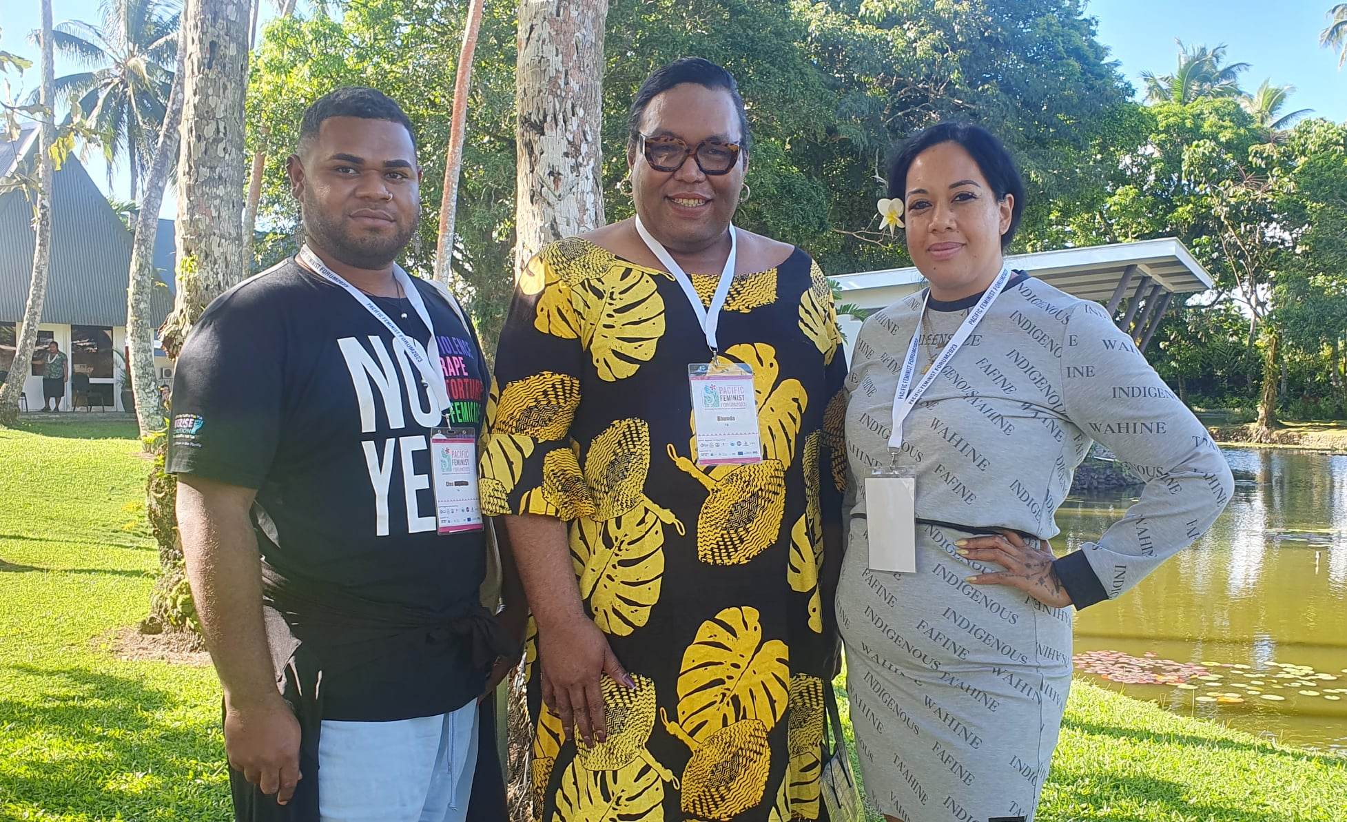 Two women and a men are standing together in a garden as they pose for the camera.
